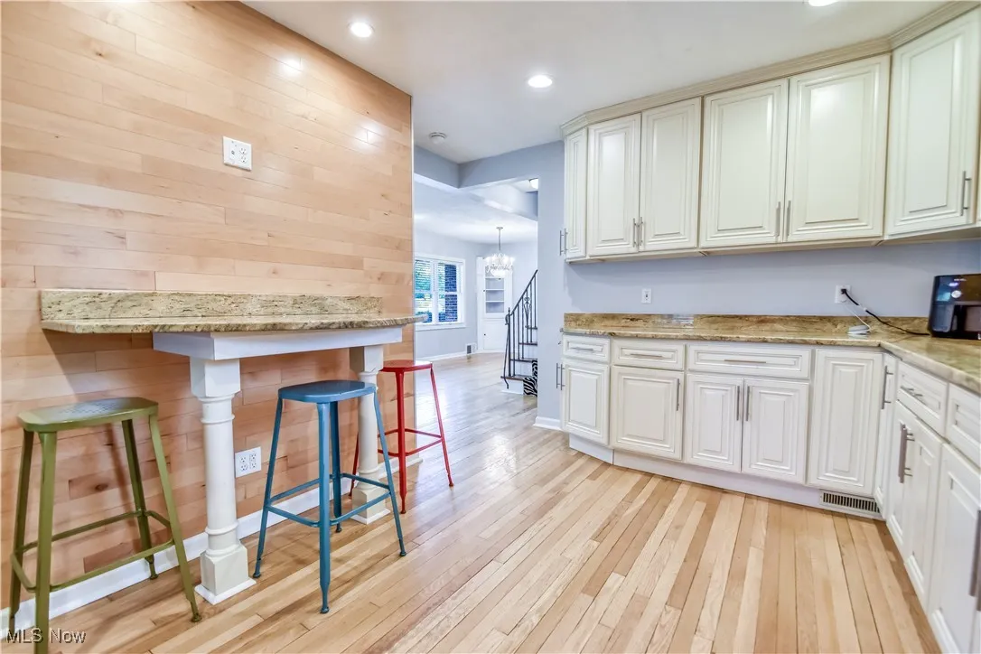 Kitchen featuring a chandelier, light wood-style floors, a breakfast bar, wood walls, and light stone counters