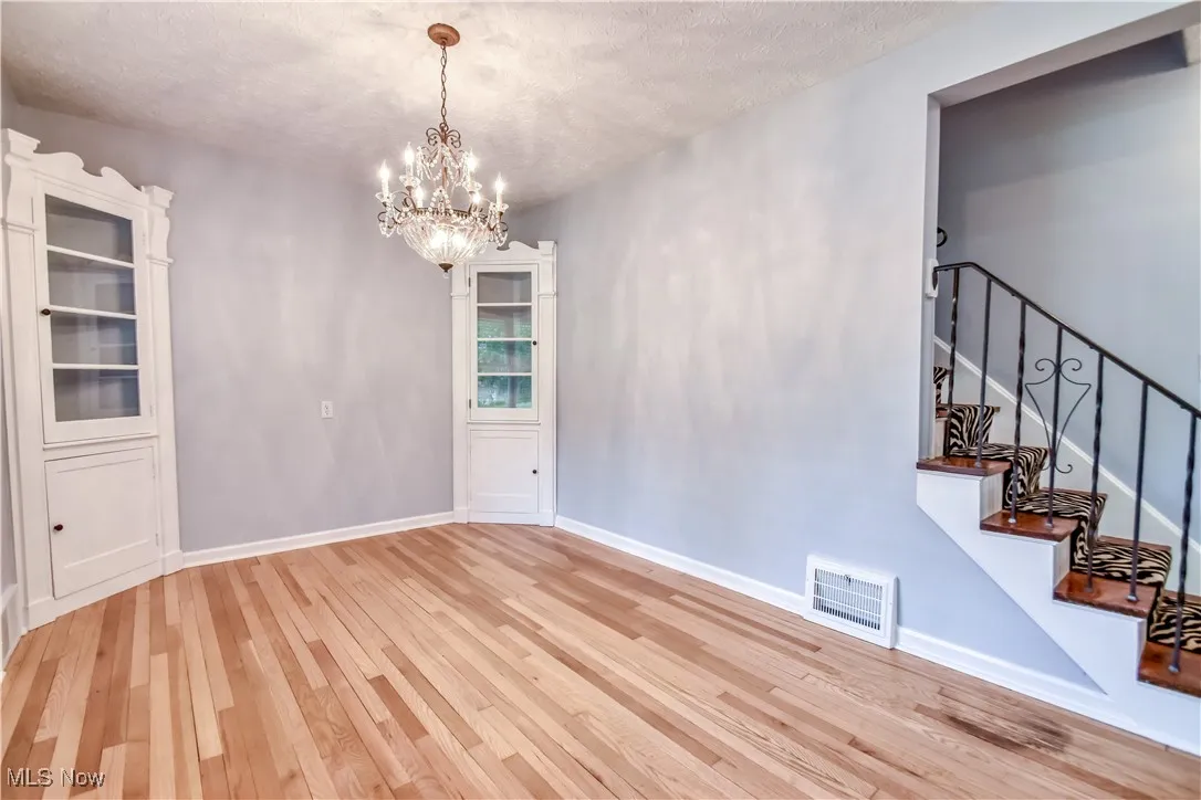 Unfurnished dining area with light wood finished floors, a chandelier, a textured ceiling, and stairway