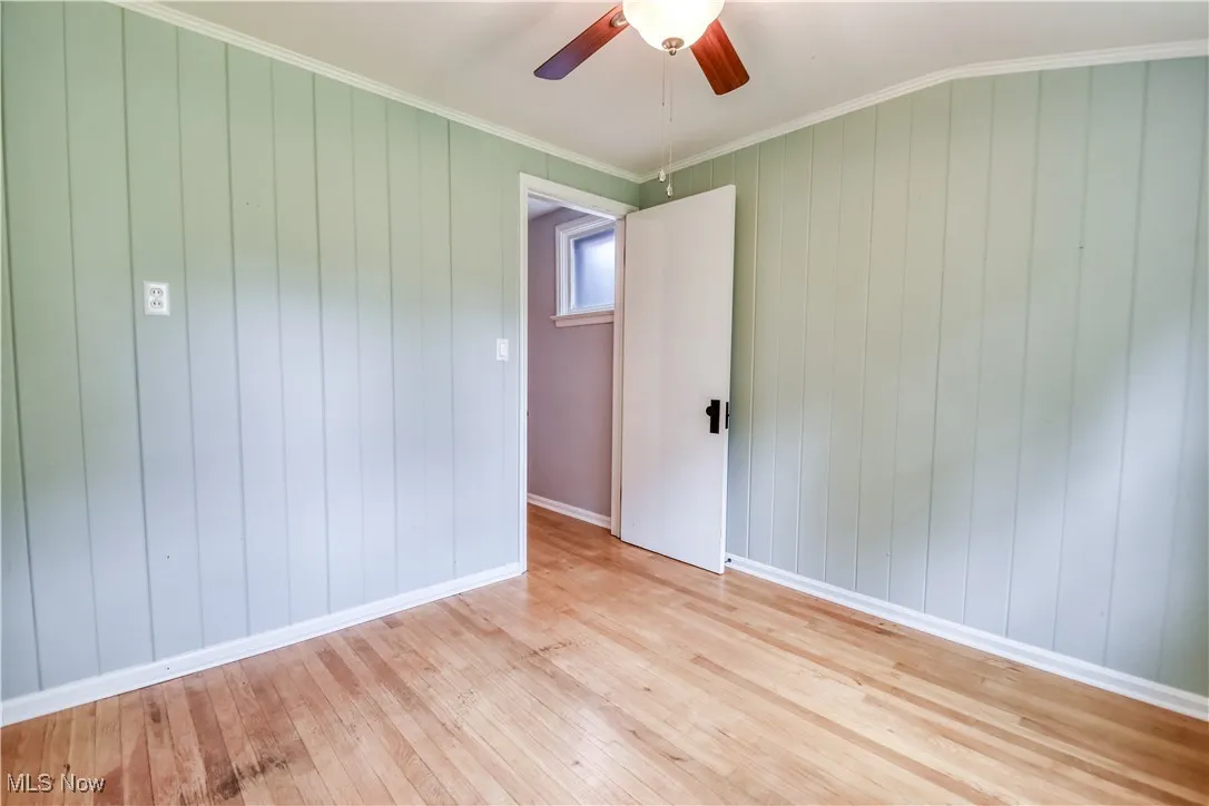 Empty room with light wood-style flooring, crown molding, ceiling fan, and wooden walls