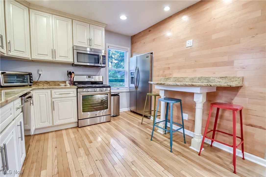 Kitchen with stainless steel appliances, light wood-style floors, wood walls, a breakfast bar area, and recessed lighting