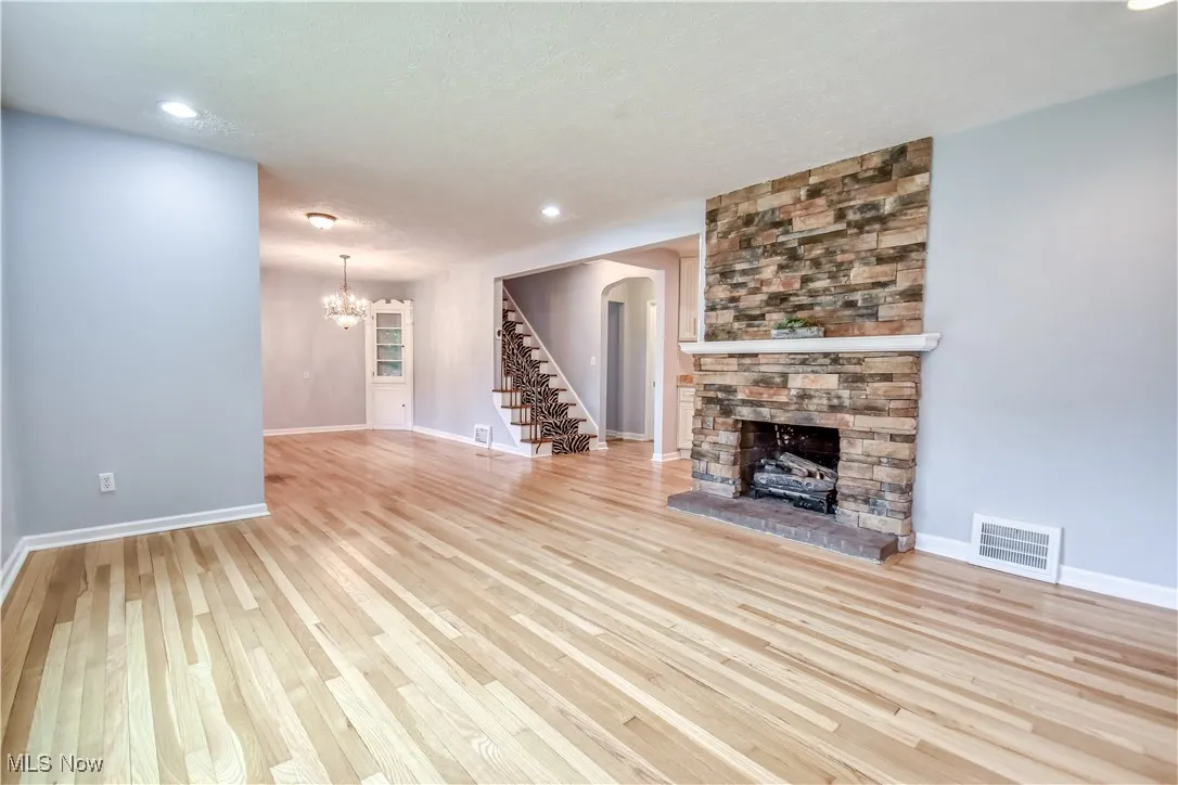 Unfurnished living room with a fireplace, a chandelier, stairs, wood finished floors, and arched walkways