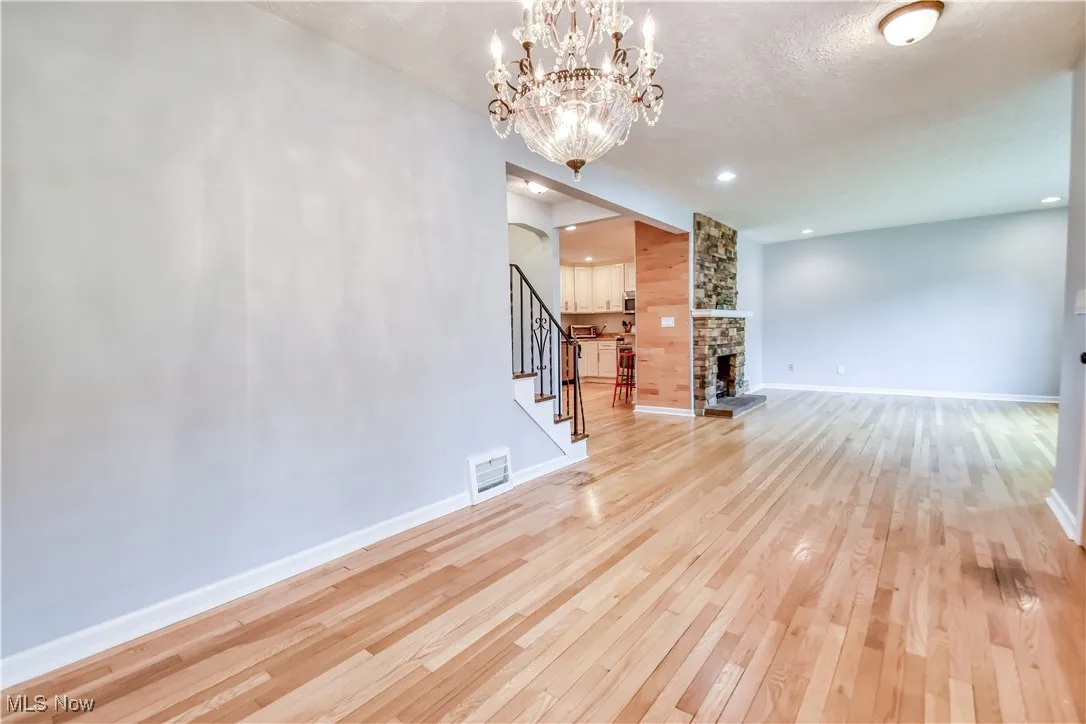 Unfurnished living room featuring light wood finished floors, stairway, a stone fireplace, a chandelier, and a textured ceiling