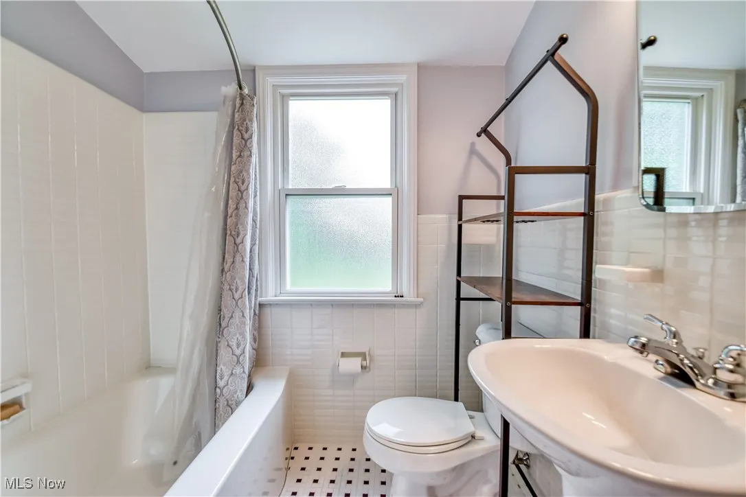 Full bath featuring tile walls, plenty of natural light, shower / bath combo, and wainscoting