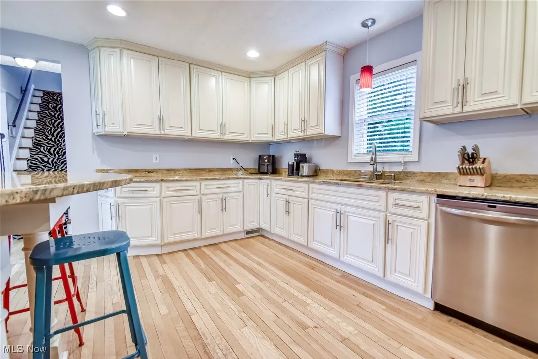 Kitchen with stainless steel dishwasher, light wood-style floors, decorative light fixtures, recessed lighting, and light stone counters