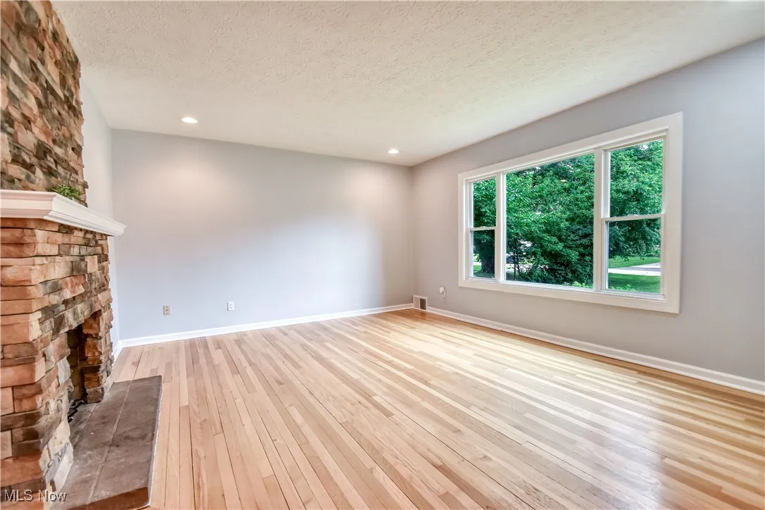 Unfurnished living room with light wood-style floors, a textured ceiling, a stone fireplace, and recessed lighting