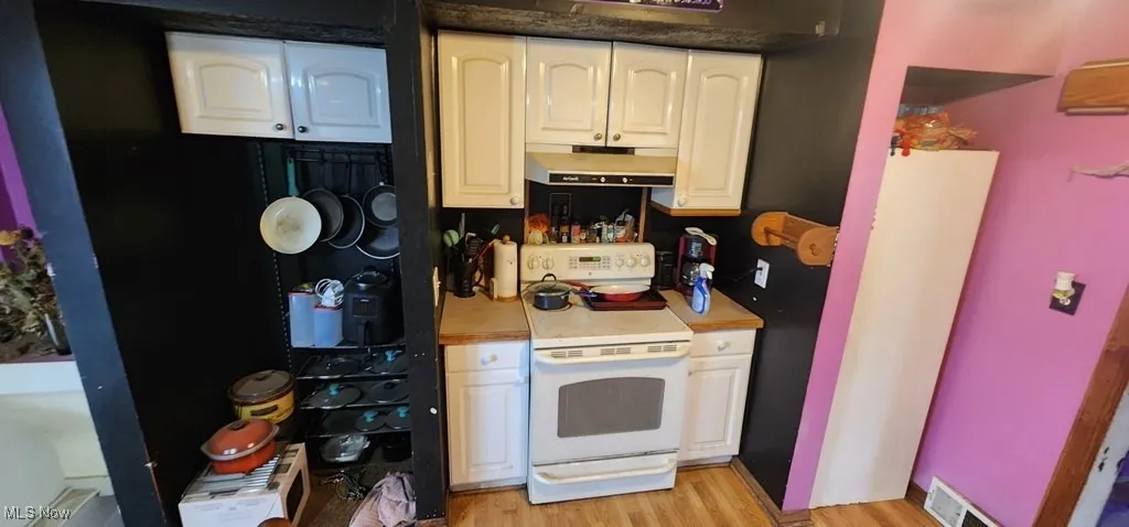 Kitchen featuring electric range, under cabinet range hood, light wood-style flooring, light countertops, and white cabinets