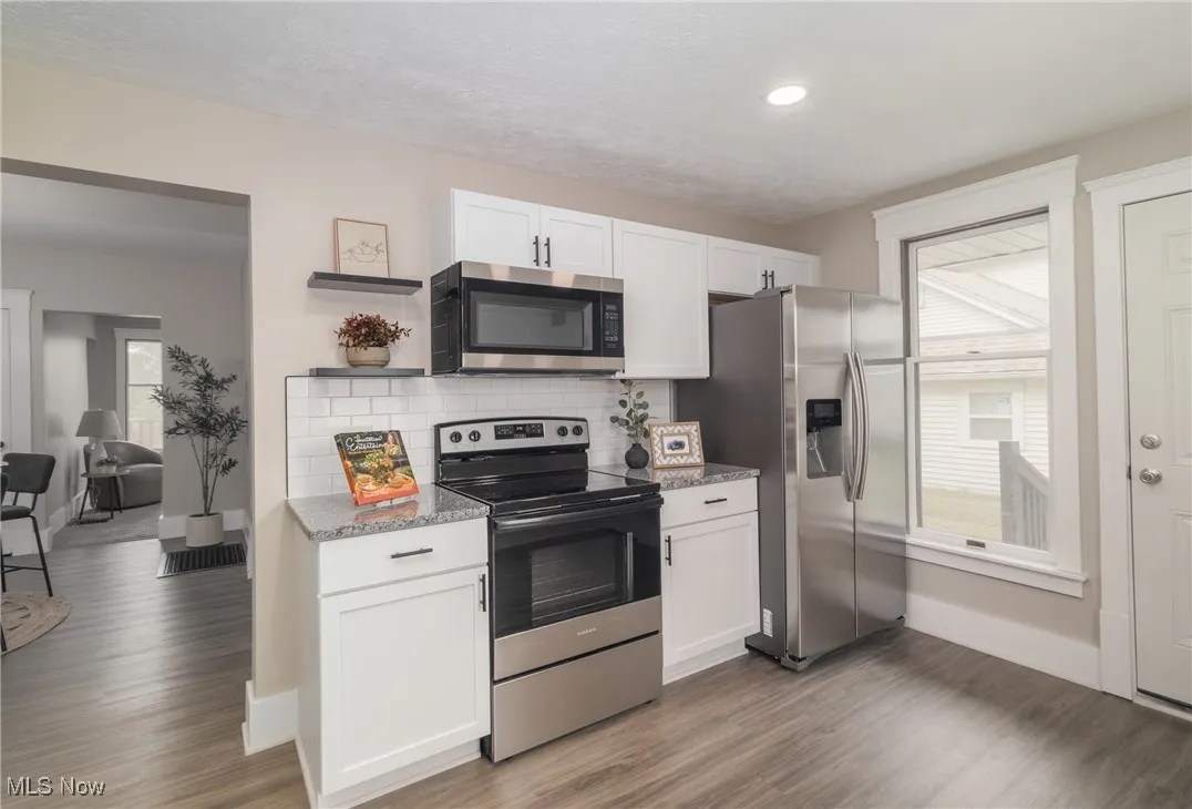 Kitchen with appliances with stainless steel finishes, open shelves, white cabinetry, light wood-type flooring, and light stone countertops