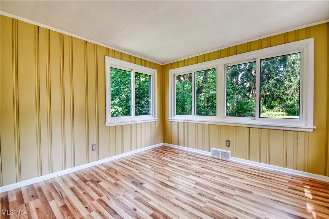 Empty room with wood finished floors, healthy amount of natural light, and ornamental molding