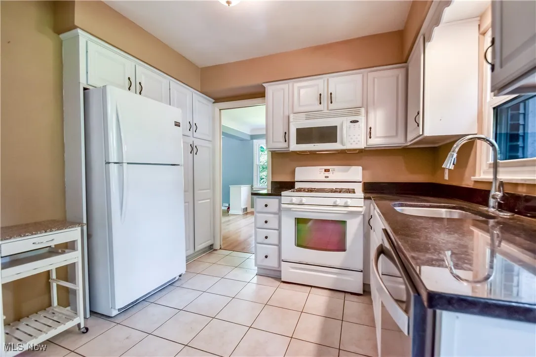 Kitchen featuring white appliances, white cabinets, and light tile patterned floors