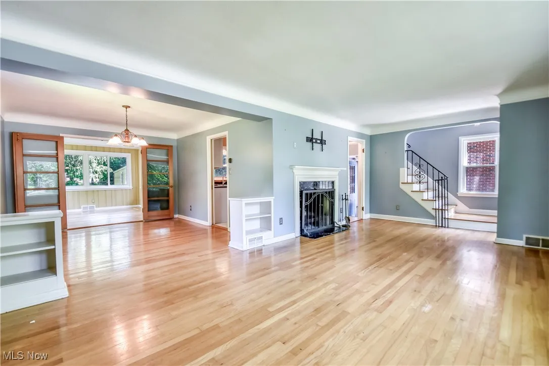 Unfurnished living room with stairs, light wood-type flooring, a premium fireplace, and a chandelier