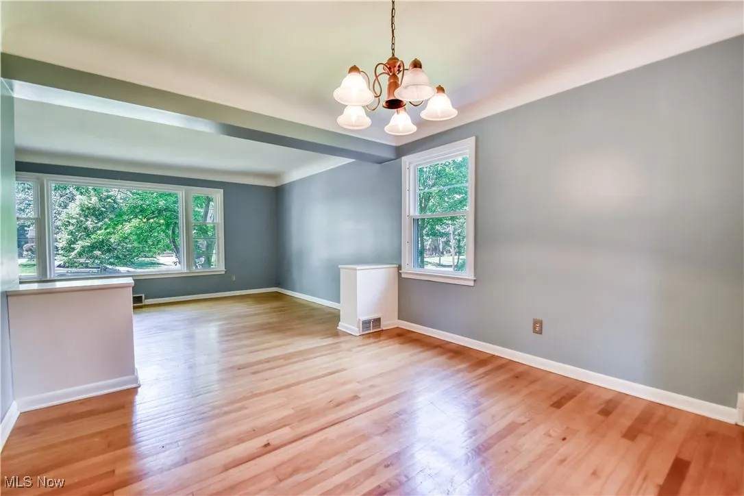 Empty room featuring healthy amount of natural light, a chandelier, and wood finished floors