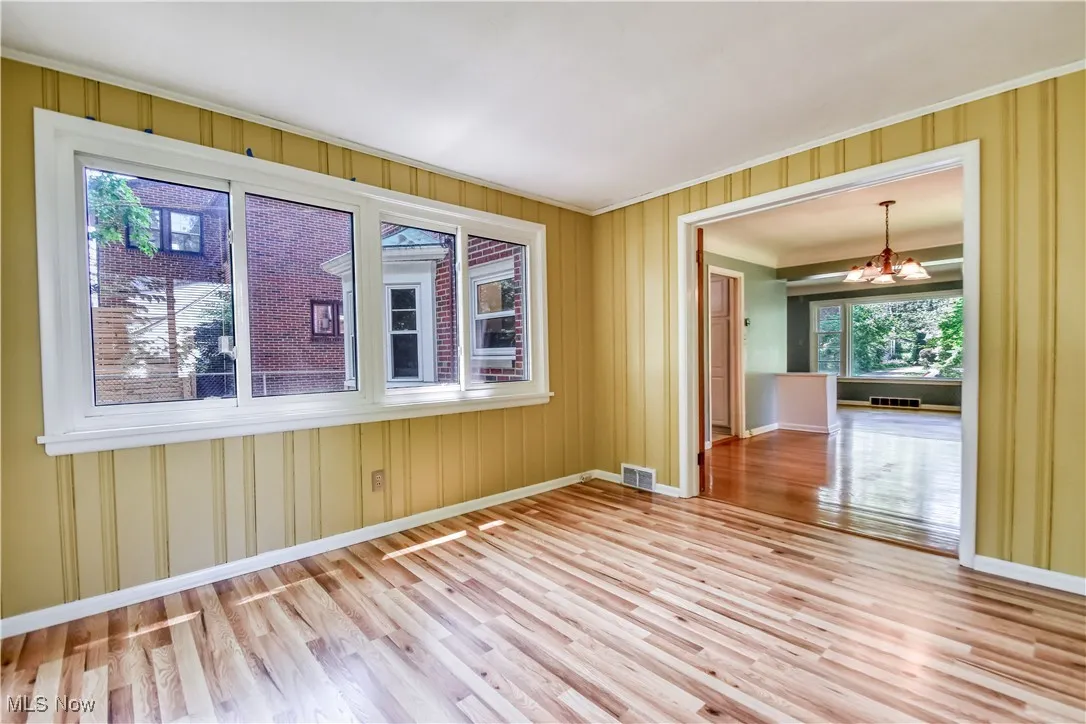 Empty room with a chandelier, wood finished floors, and ornamental molding