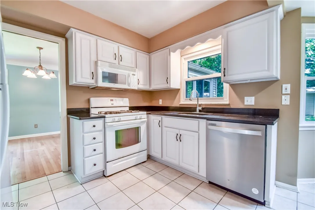 Kitchen featuring white appliances, dark countertops, white cabinets, and a chandelier
