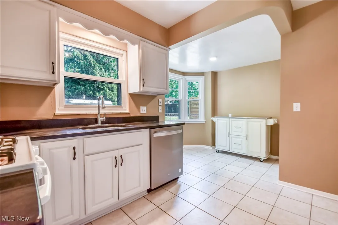 Kitchen with stainless steel dishwasher, dark countertops, range, and white cabinets