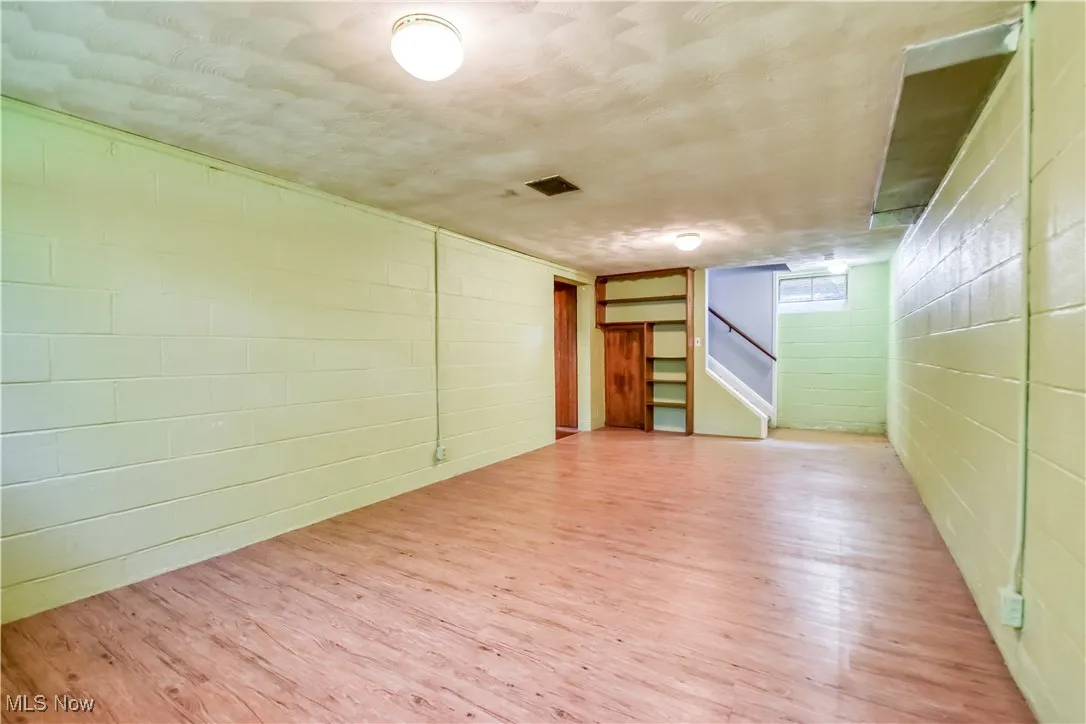 Empty room with wood finished floors, stairway, and concrete block wall
