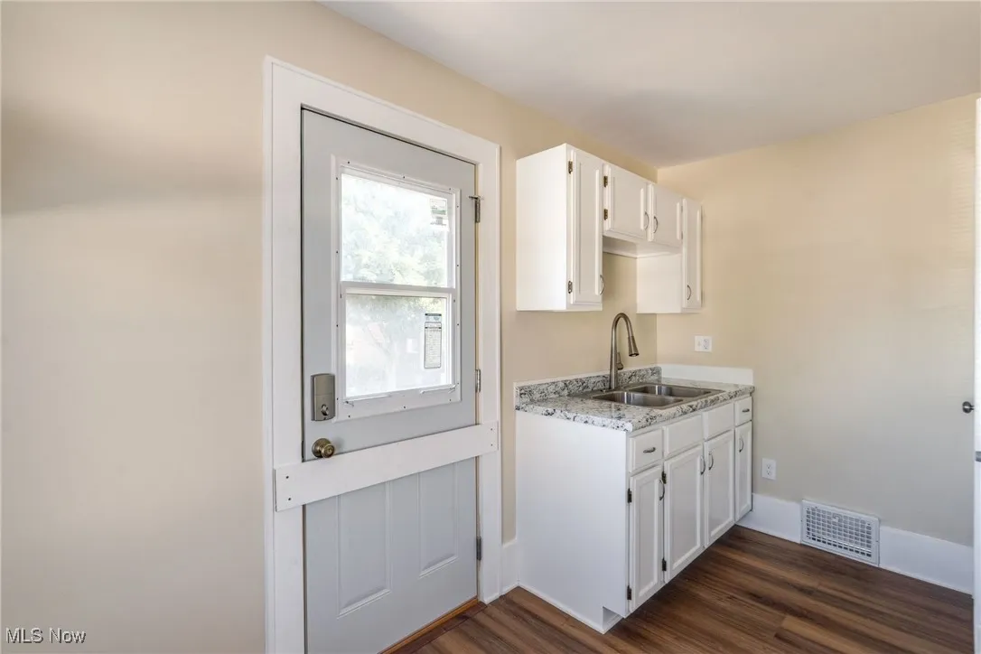 Kitchen with dark wood-style flooring, white cabinets, and light stone counters