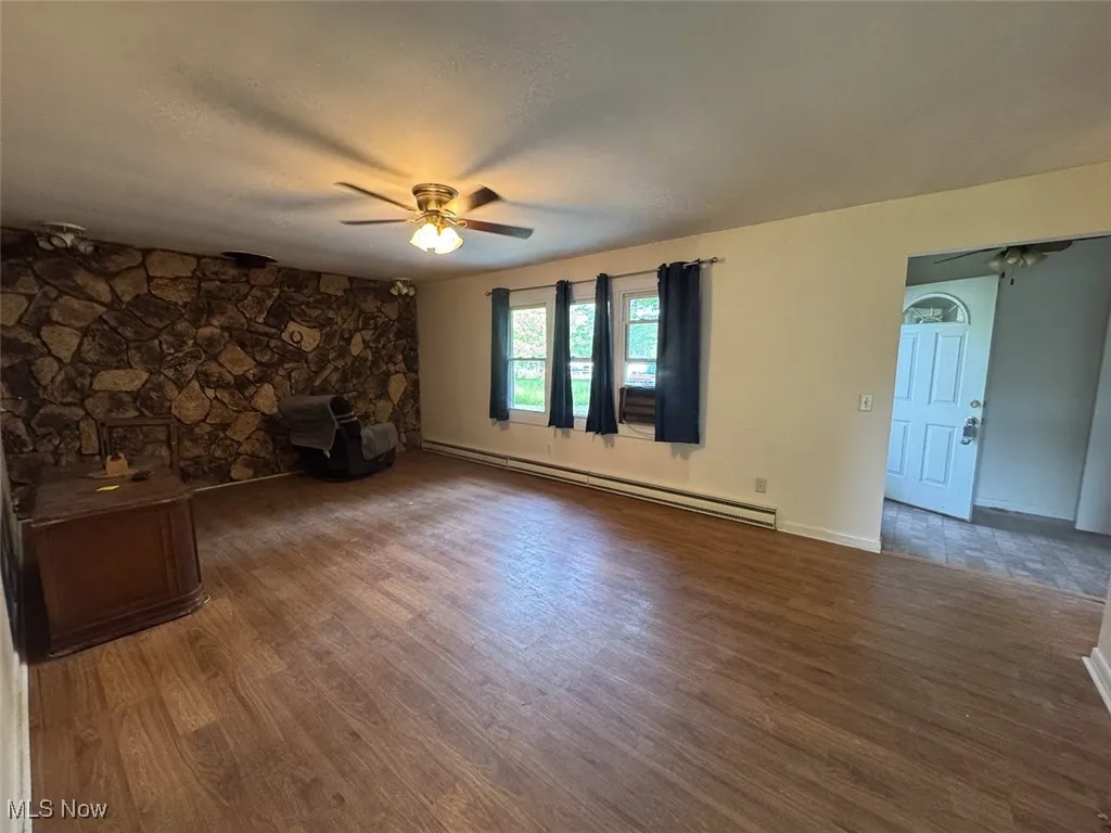 Unfurnished living room with a baseboard radiator, a ceiling fan, and wood finished floors