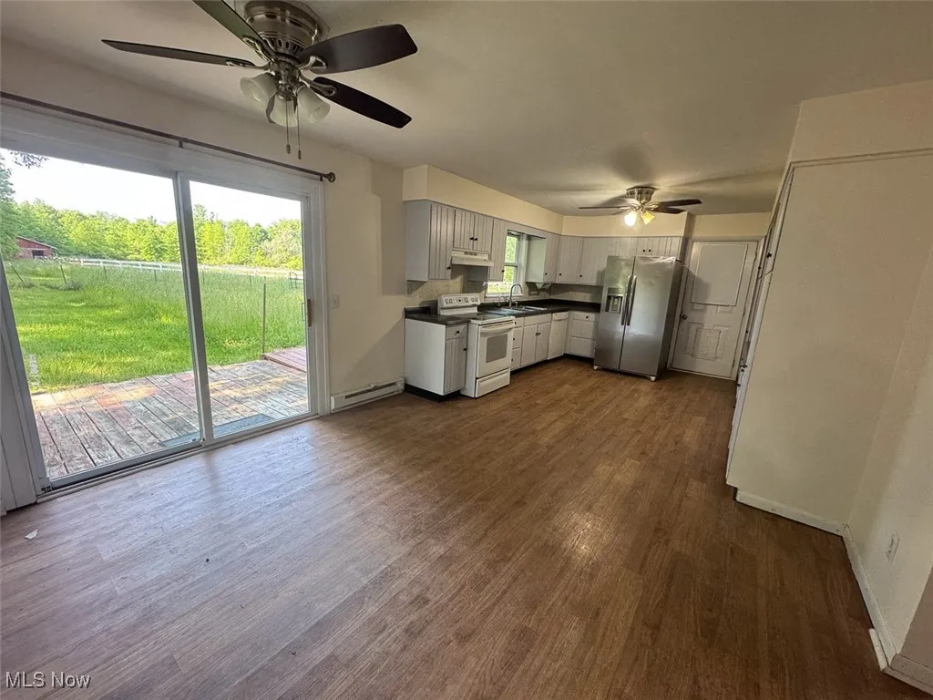 Kitchen with white range with electric stovetop, a ceiling fan, stainless steel fridge with ice dispenser, dark countertops, and dark wood-style floors