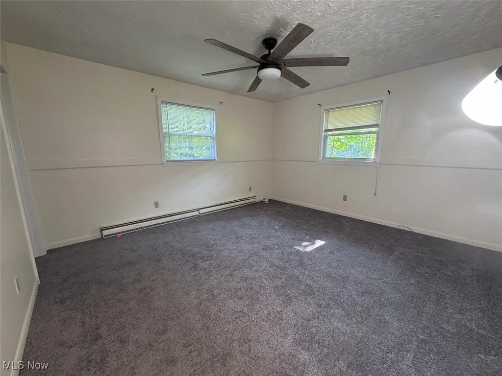 Bedroom with baseboard heating, plenty of natural light, dark colored carpet, ceiling fan, and a textured ceiling