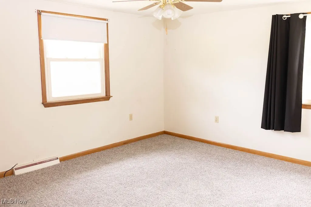 Empty room with carpet flooring, baseboard heating, and a ceiling fan