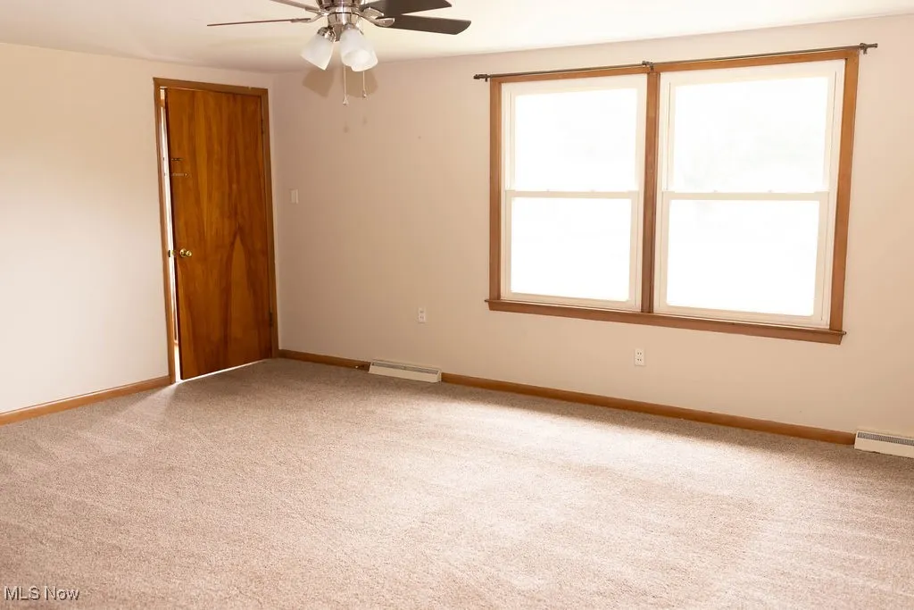 Carpeted spare room with ceiling fan, plenty of natural light, and a baseboard heating unit