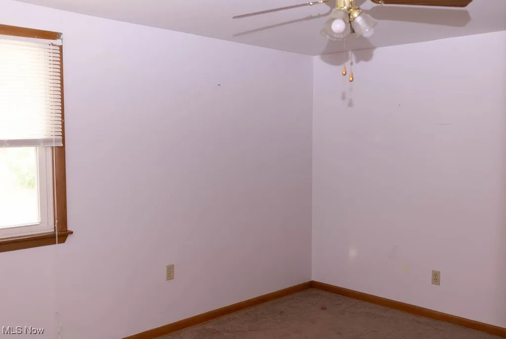 Carpeted empty room with a ceiling fan and baseboards