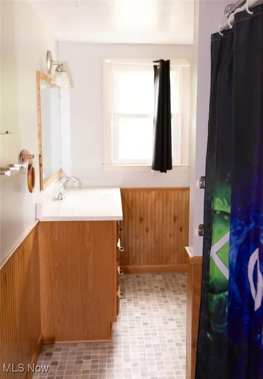 Bathroom with vanity, a wainscoted wall, wooden walls, and curtained shower