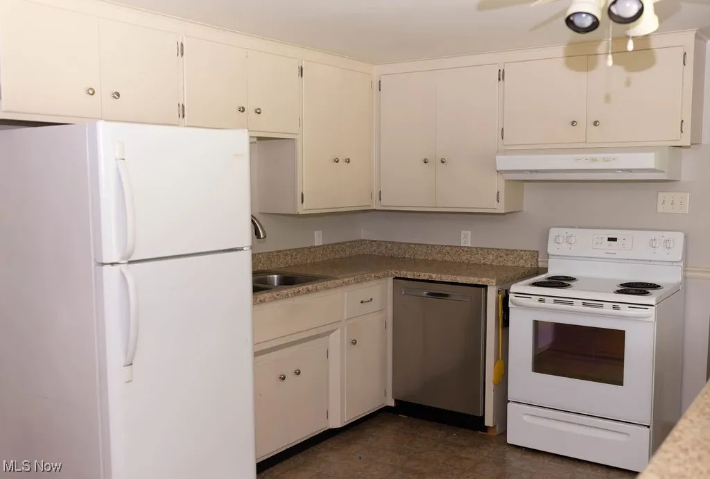 Kitchen with white appliances, under cabinet range hood, dark flooring, light countertops, and white cabinetry