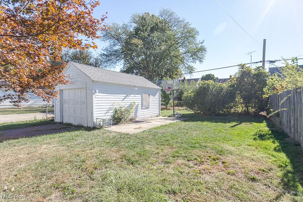 Fenced backyard featuring a detached garage, an outdoor structure, and driveway