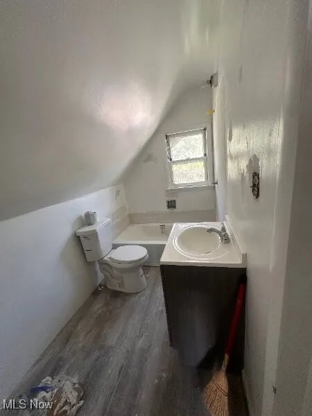 Bathroom with vaulted ceiling, wood finished floors, a bathtub, and vanity