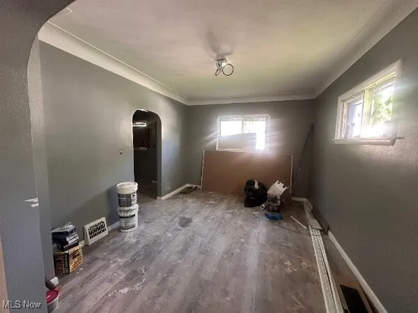 Unfurnished dining area featuring arched walkways, crown molding, and wood finished floors