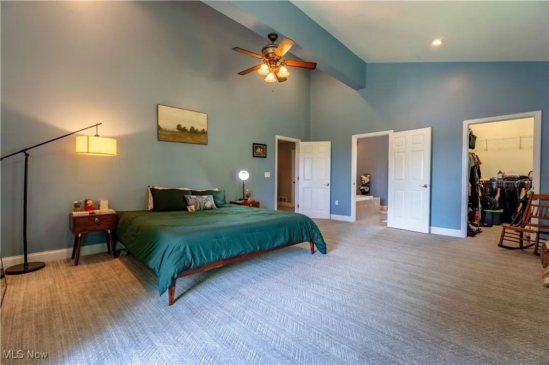 Bedroom featuring carpet floors, a walk in closet, high vaulted ceiling, beamed ceiling, and ensuite bath