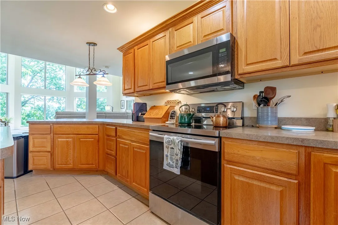 Kitchen featuring appliances with stainless steel finishes, light tile patterned flooring, light countertops, hanging light fixtures, and a peninsula