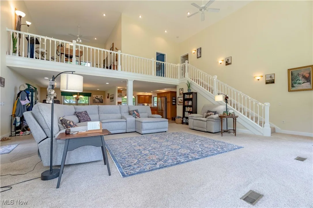 Carpeted living area featuring ceiling fan, a high ceiling, stairs, and recessed lighting