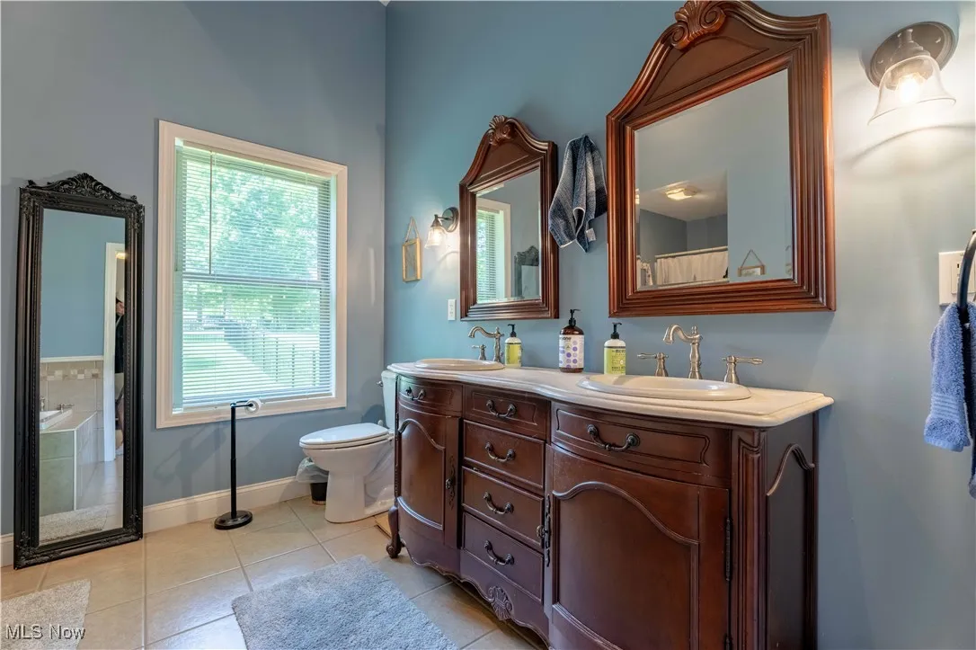 Full bath featuring double vanity, tile patterned flooring, and a tub to relax in