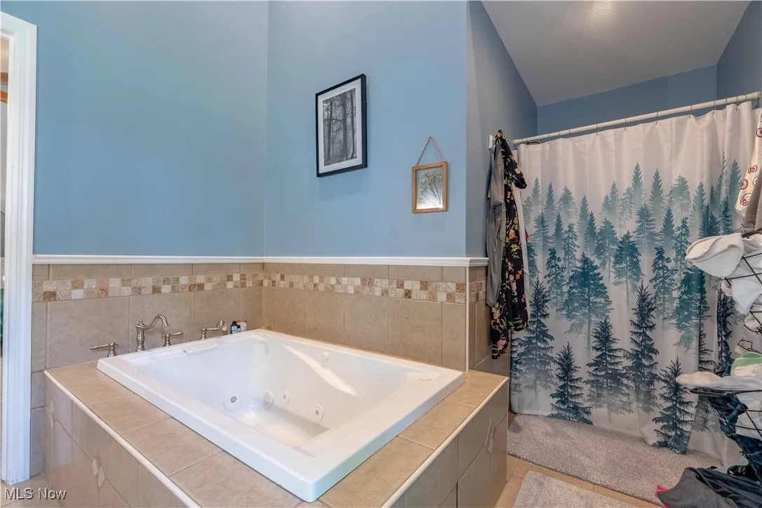 Bathroom featuring a jetted tub, a shower with curtain, and tile patterned floors