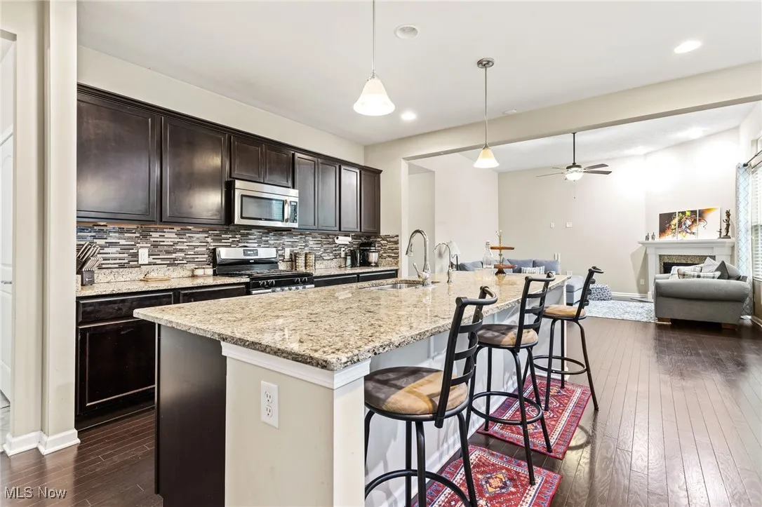 Kitchen featuring appliances with stainless steel finishes, dark wood-style floors, backsplash, open floor plan, and a breakfast bar