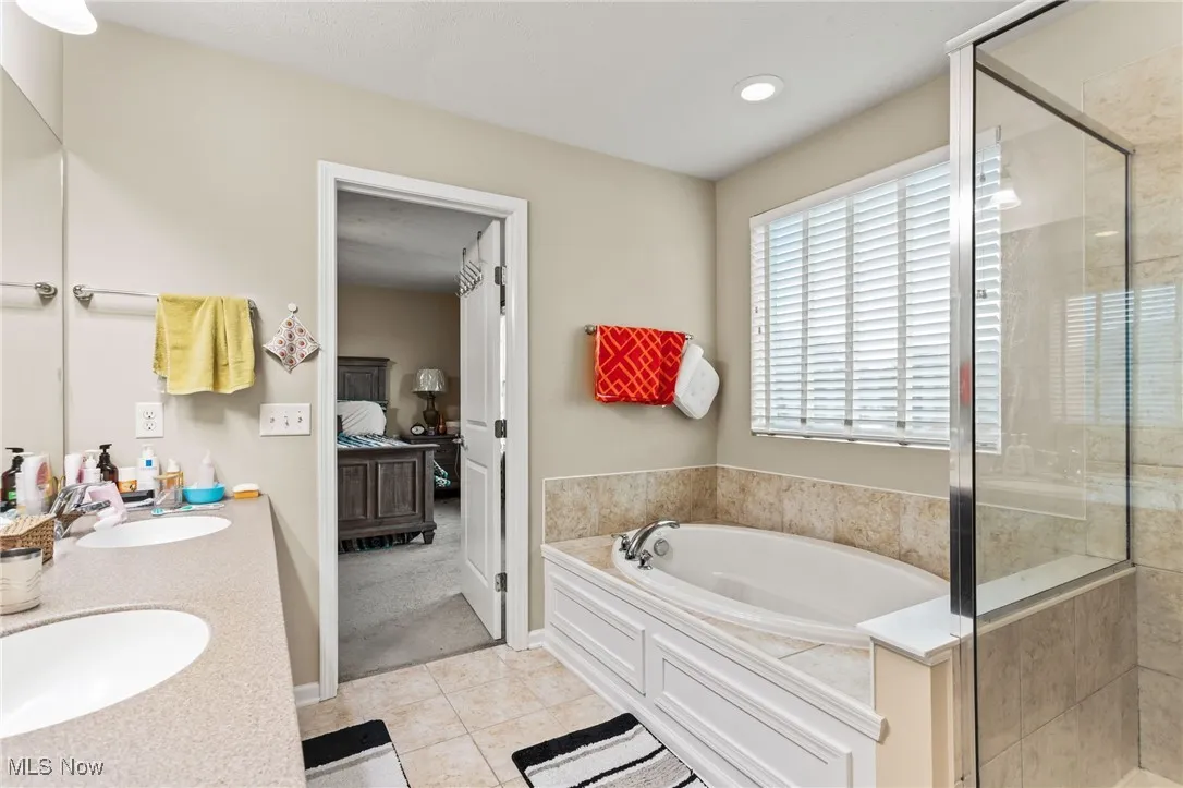 Bathroom featuring ensuite bathroom, a bath, tile patterned floors, double vanity, and a shower stall
