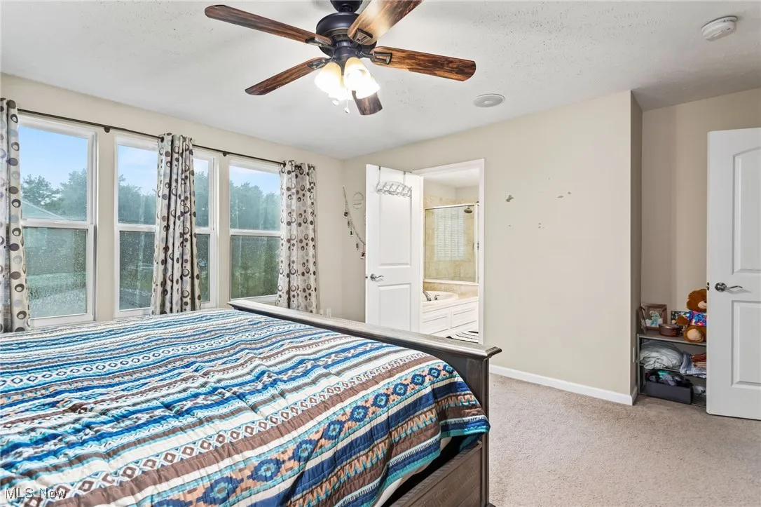 Carpeted bedroom with a textured ceiling, ceiling fan, and connected bathroom