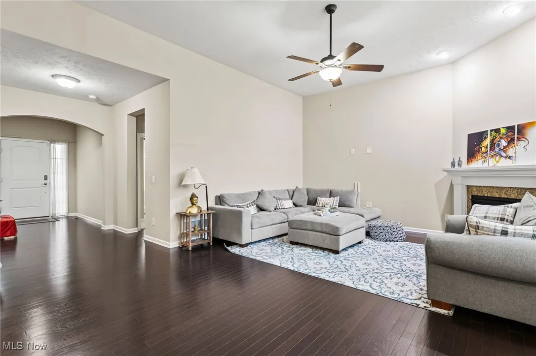 Living room with arched walkways, a ceiling fan, a fireplace, and wood finished floors