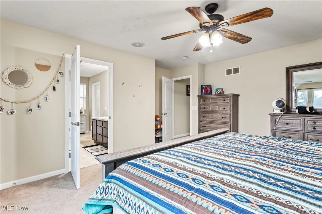 Bedroom featuring light carpet, ensuite bath, and a ceiling fan