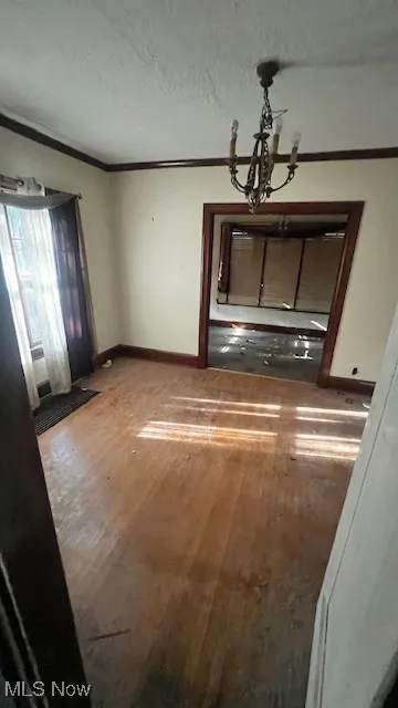 Unfurnished living room with crown molding, light wood-style floors, a chandelier, and a textured ceiling