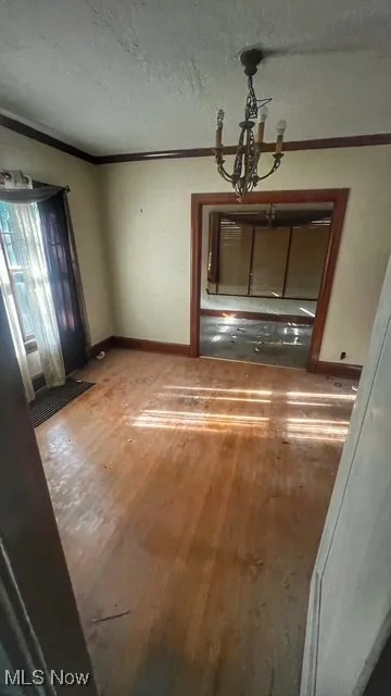 Unfurnished dining area featuring light wood-style flooring, ornamental molding, a chandelier, and a textured ceiling