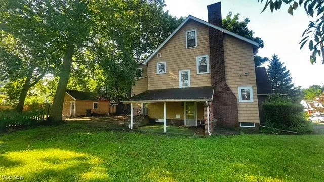 Rear view of property featuring a chimney, a yard, covered porch, and an outbuilding