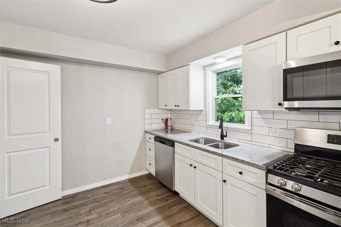 Kitchen featuring appliances with stainless steel finishes, tasteful backsplash, dark wood-type flooring, white cabinetry, and light stone counters