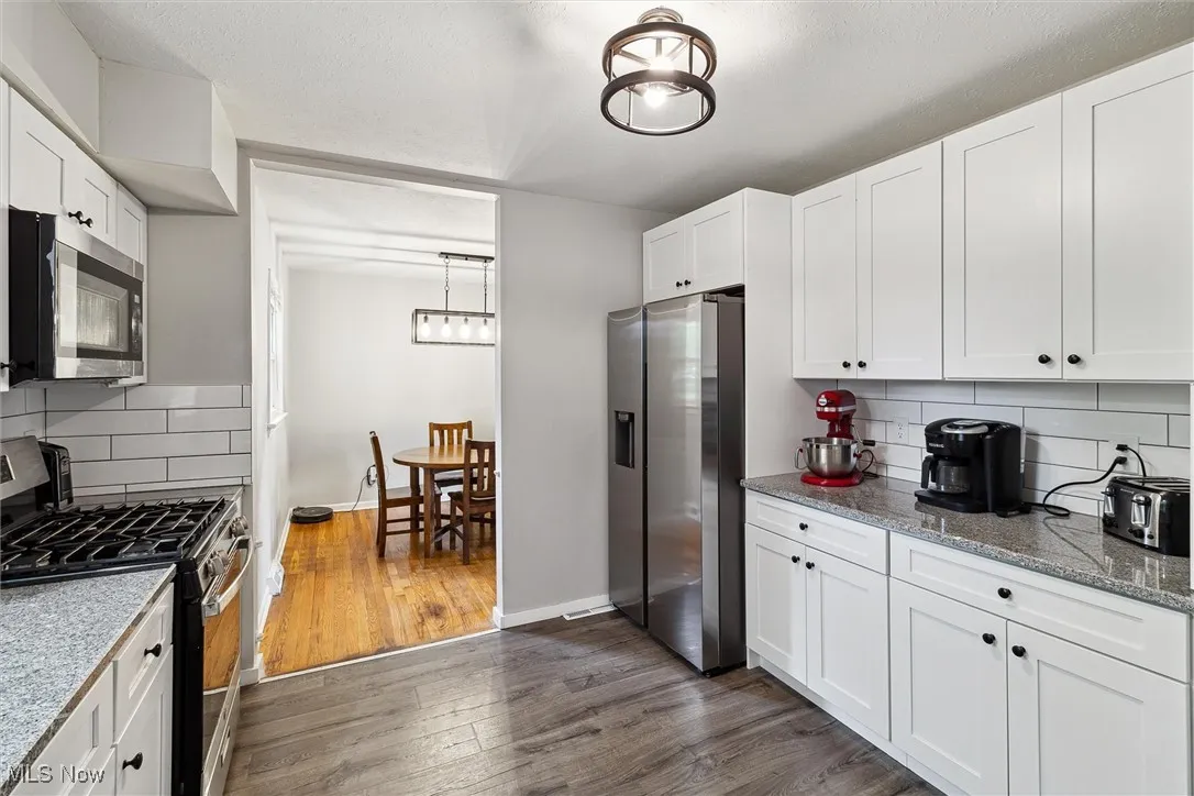 Kitchen featuring stainless steel appliances, dark wood-style flooring, backsplash, white cabinetry, and light stone countertops