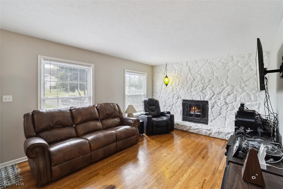 Living room with wood finished floors, a stone fireplace, and a textured ceiling