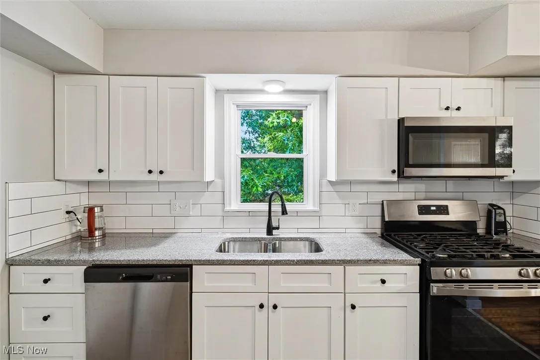 Kitchen with appliances with stainless steel finishes, white cabinetry, decorative backsplash, and light stone counters