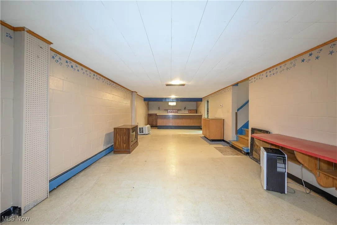 Finished below grade area with light flooring, baseboard heating, ornamental molding, and concrete block wall