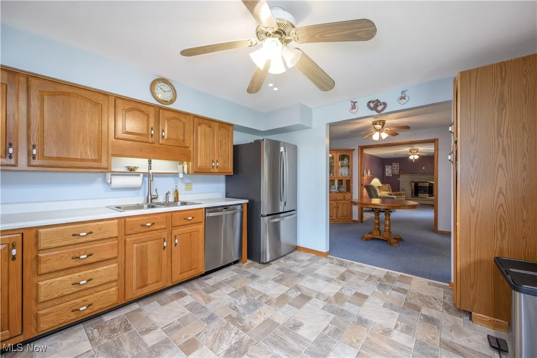 Kitchen featuring stainless steel appliances, ceiling fan, light countertops, brown cabinetry, and light stone finish flooring